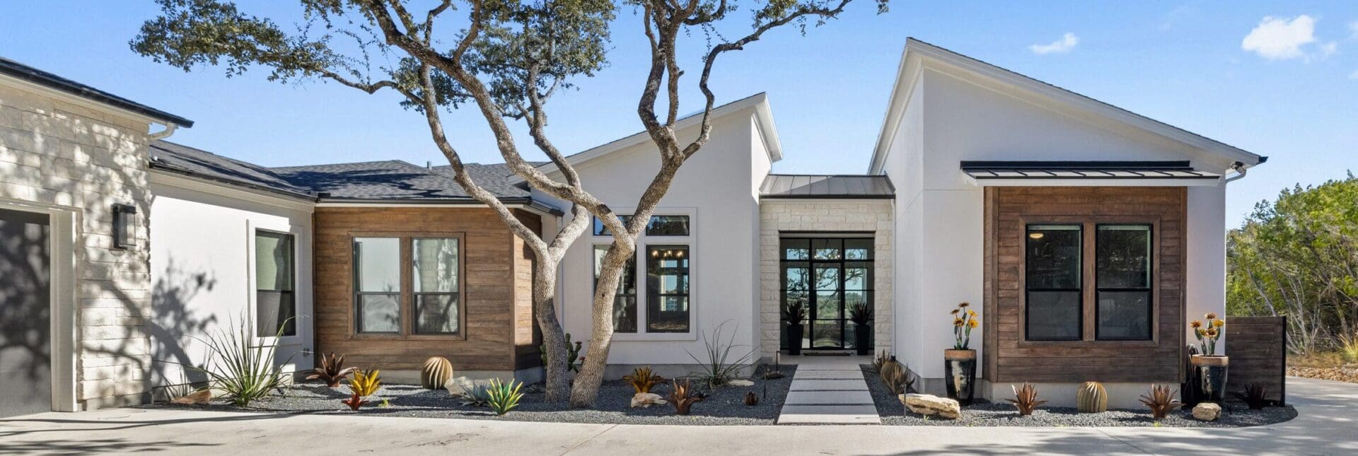 Modern exterior of a single-story home with large windows and a tree in front.