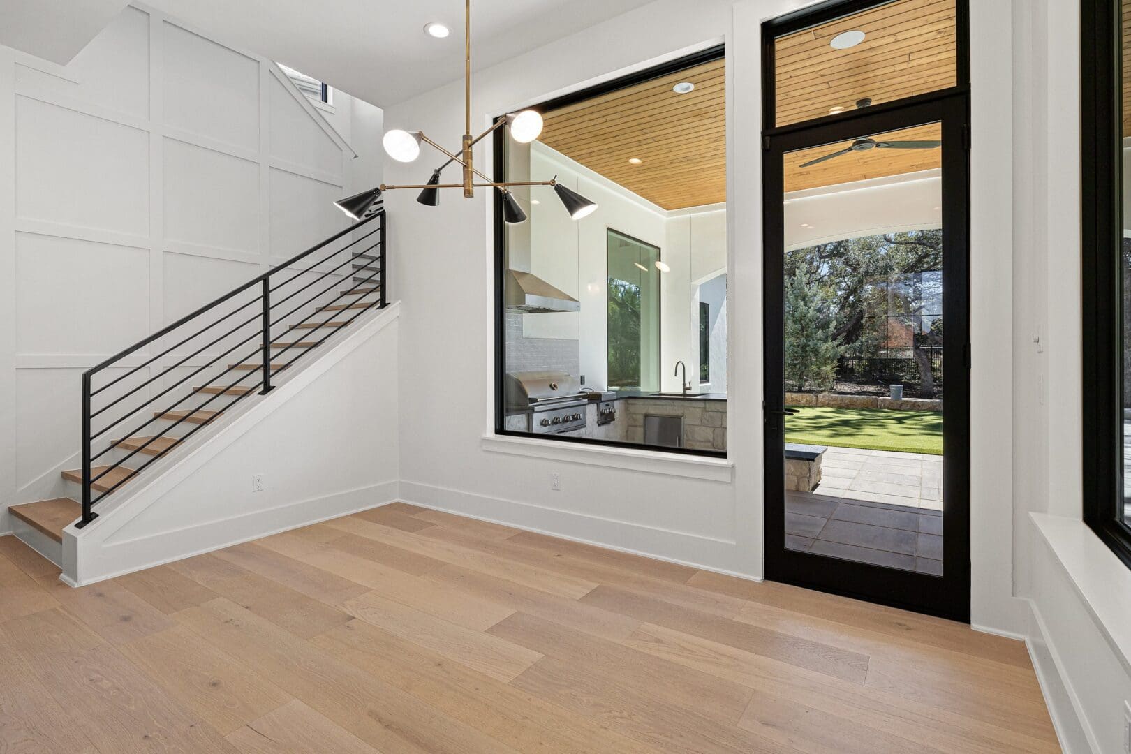 Modern empty room with wooden floor and large window overlooking garden.