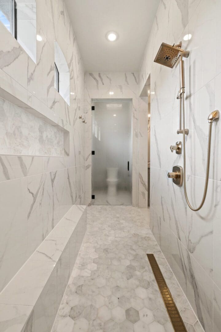 Modern white marble bathroom with walk-in shower and built-in bench.