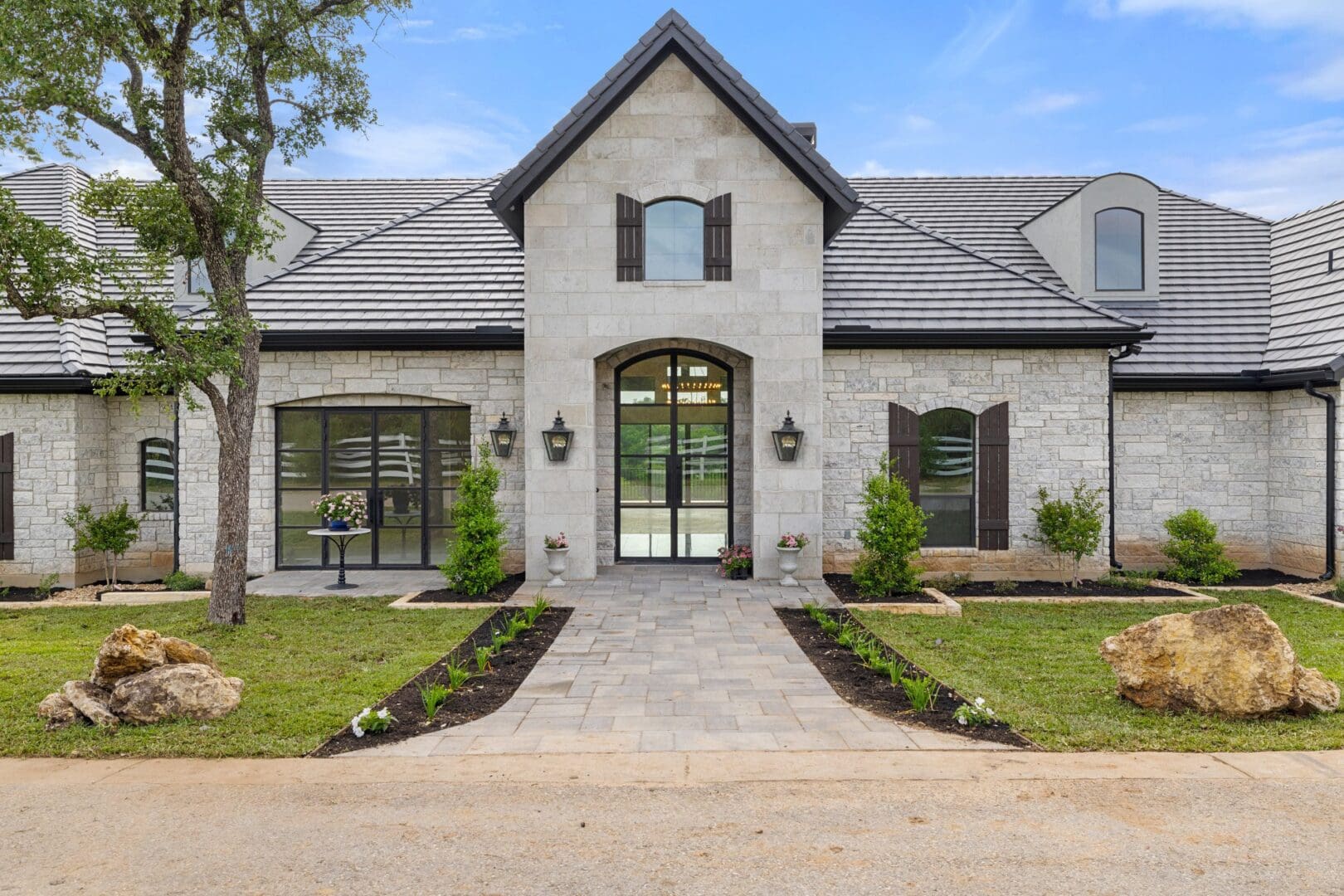 Elegant stone house with symmetrical landscaping and large windows.