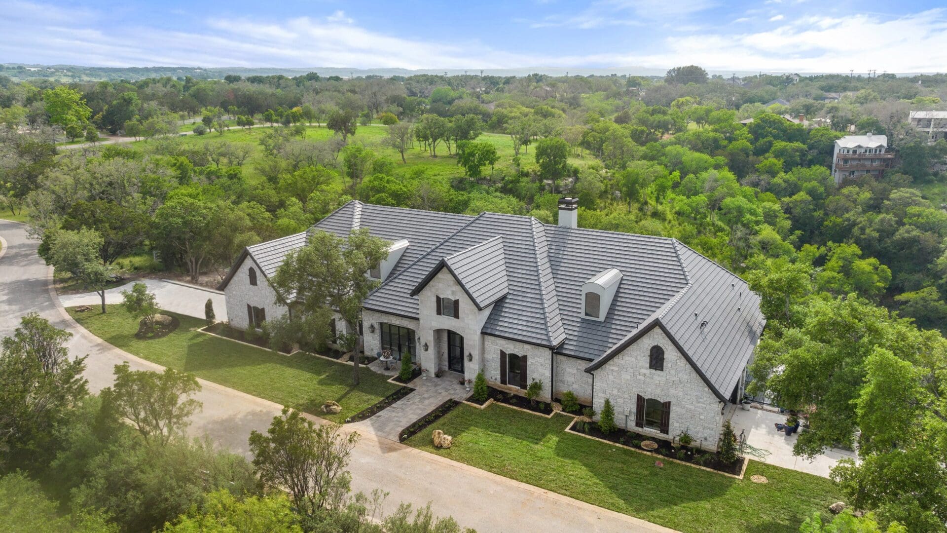 Large modern house with a gray roof surrounded by greenery.