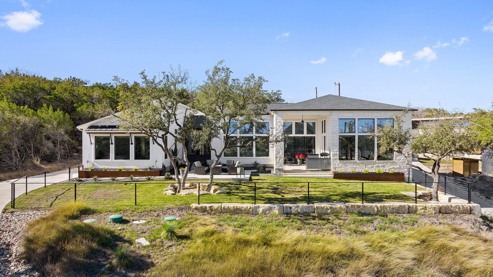 A modern white building with large windows in a natural, grassy setting under a clear blue sky.