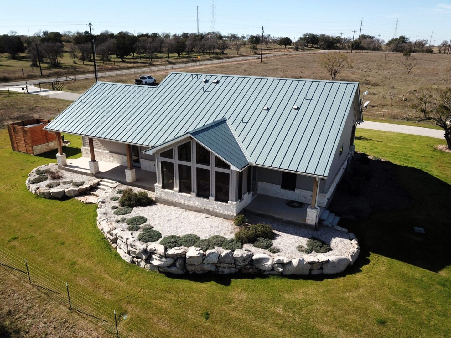 Modern house with metal roof and stone landscaping on a spacious lawn.