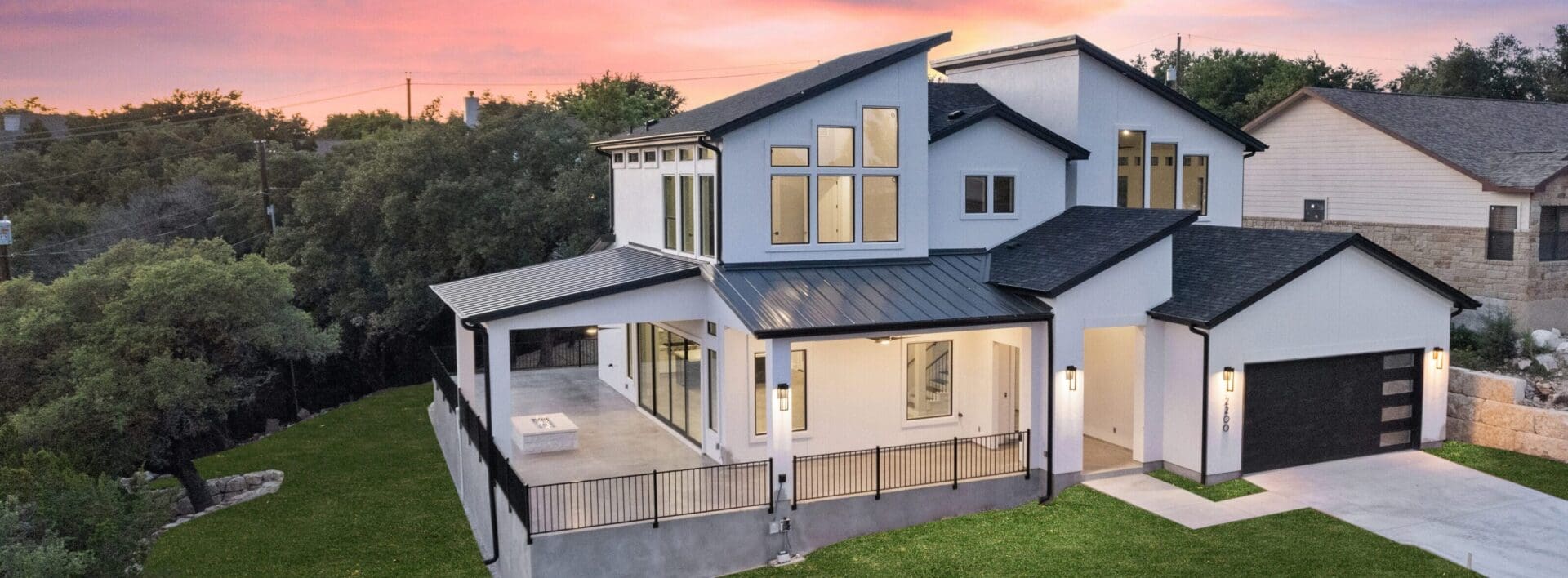 Modern two-story house with large windows and a spacious balcony at sunset.
