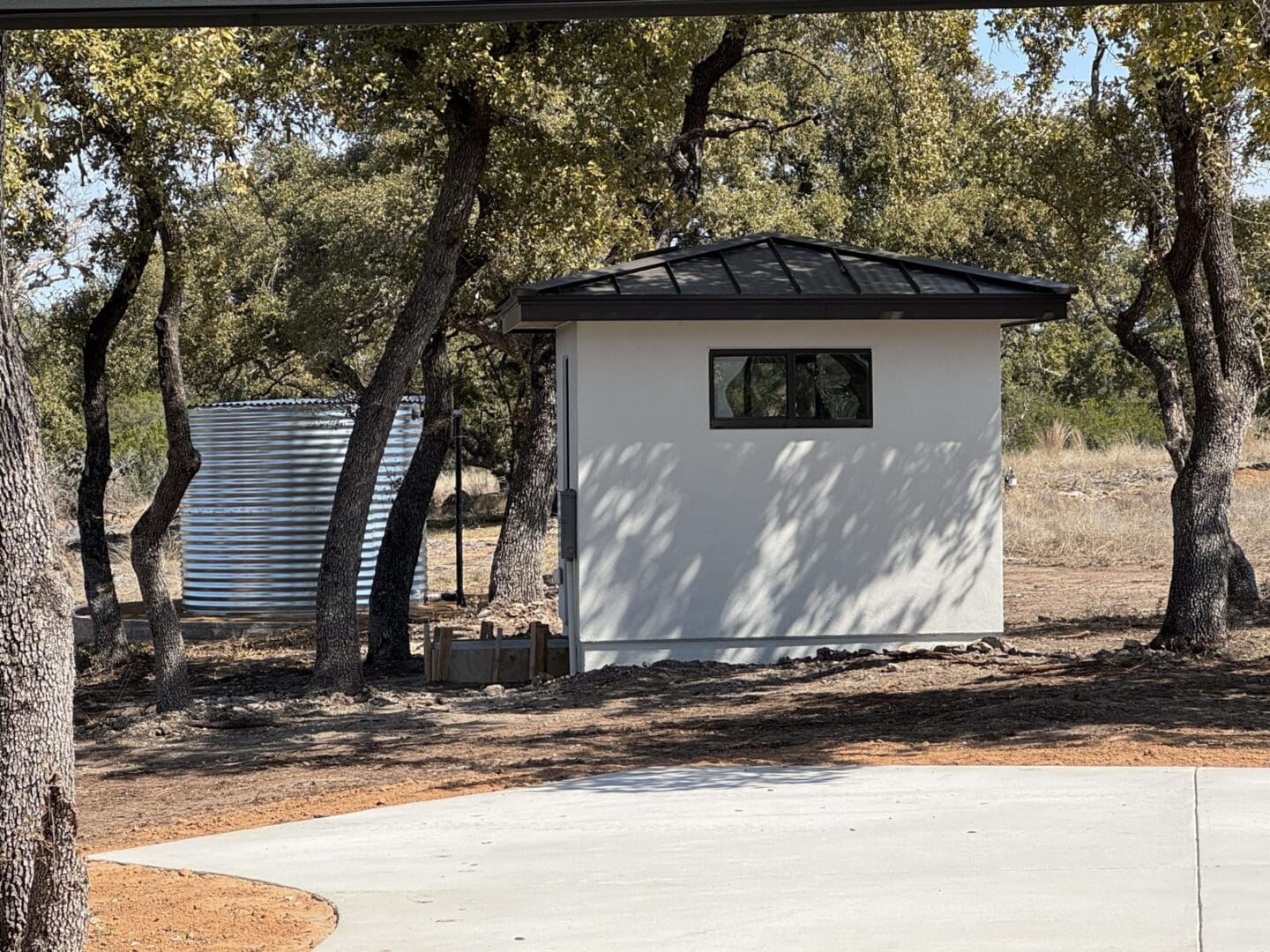 Small white utility building beside a larger metal tank in a wooded area.