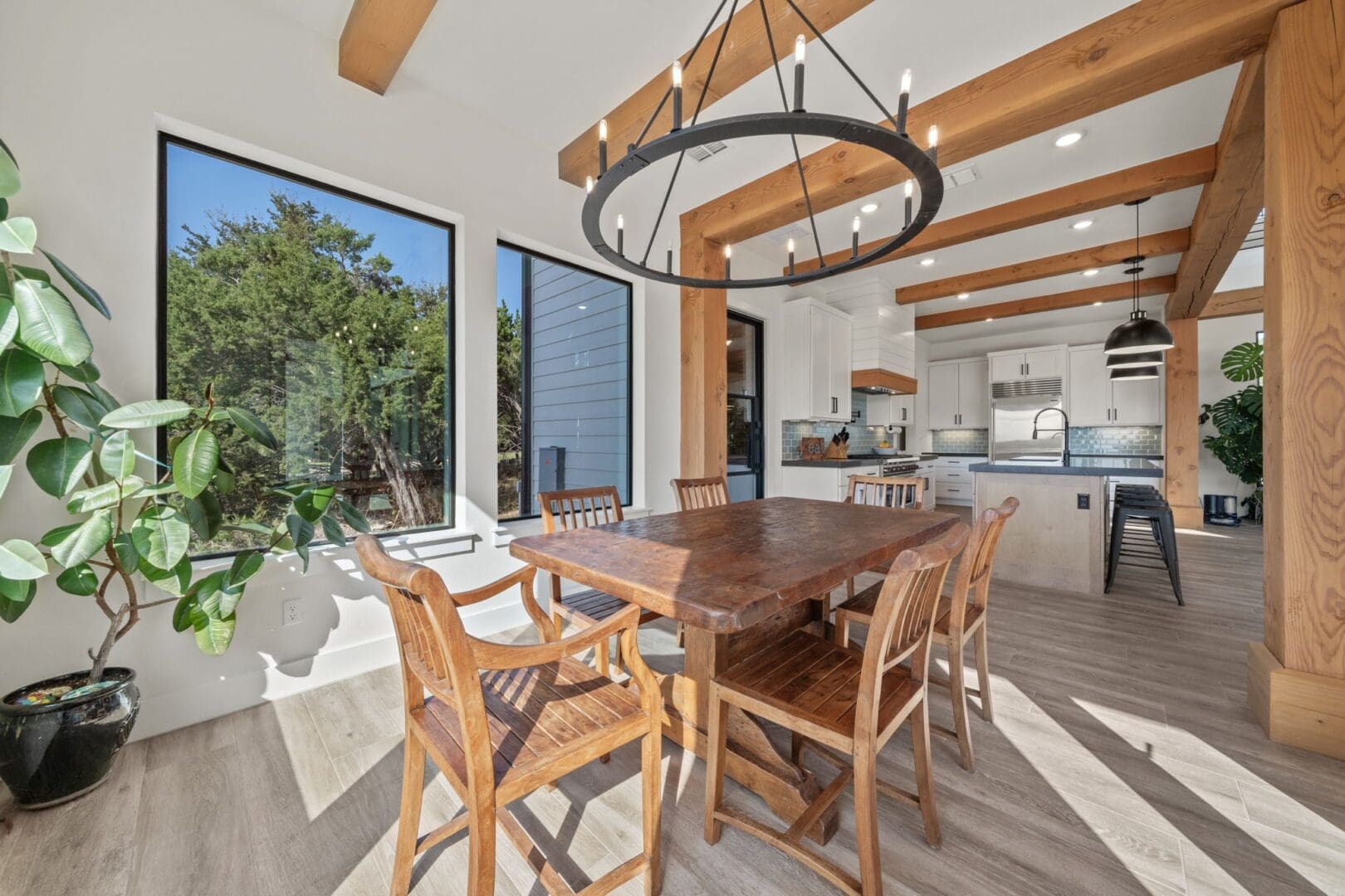 Modern dining area with wooden table and large windows overlooking greenery.